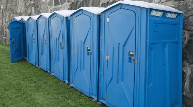 Row of blue portable toilets lined up on grass against a stone wall for event sanitation in Mobile, AL