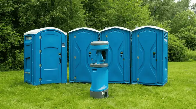 Four blue portable toilets and a matching hand washing station on grass near trees, a common sight at local outdoor events in Mobile, AL