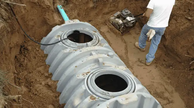 Septic tank installation showing a technician compacting soil around a new poly septic tank in an excavation pit in Mobile, AL